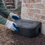 Village Green technician placing a tamper-resistant rodent bait station along the foundation of a brick home